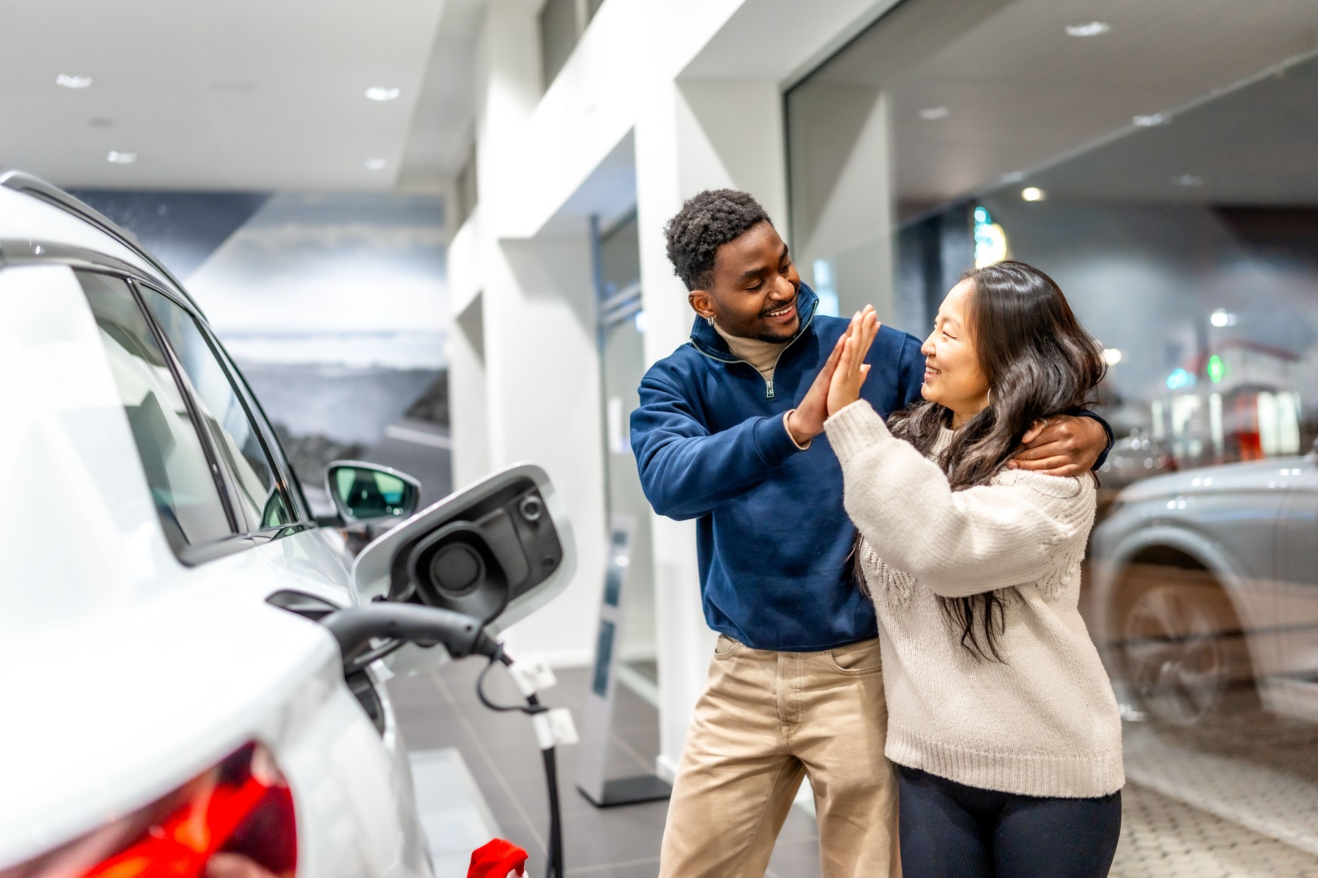 Happy multiethnic couple celebrating buying electric car at dealership